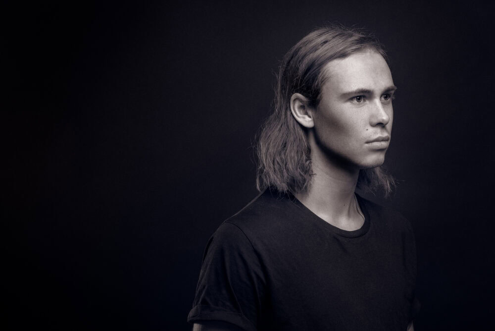 A man with long hair and a black shirt. Portrait shot in a photo studio.