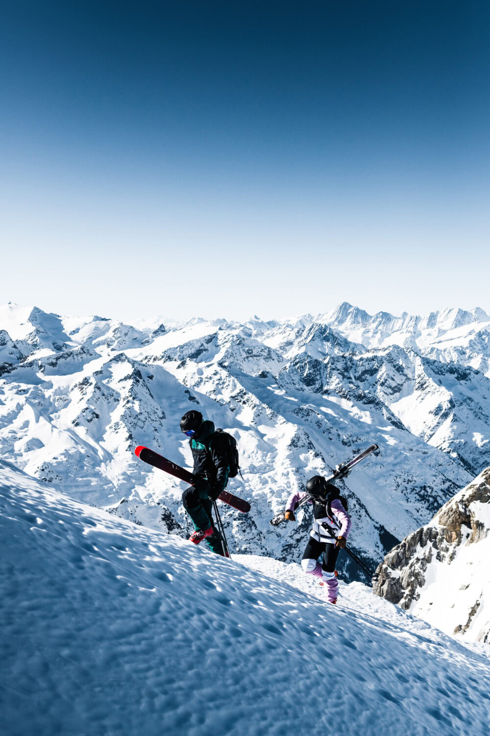 Two people with skis on a snowy mountain. J.Lindeberg Ski fall/winter 21. Campaign photographed by Axel Adolfsson.
