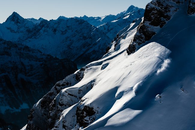 Marco Burch making turns outside of the resort Melchsee-Frutt. Snow-covered mountain peaks with dramatic shadows and clear blue sky, landscape photography by Axel Adolfsson, winter mountain scenery, alpine wilderness, nature photography.