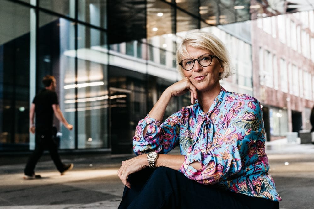A woman with glasses sitting on the ground in front of a building. Elisabeth Svantesson.