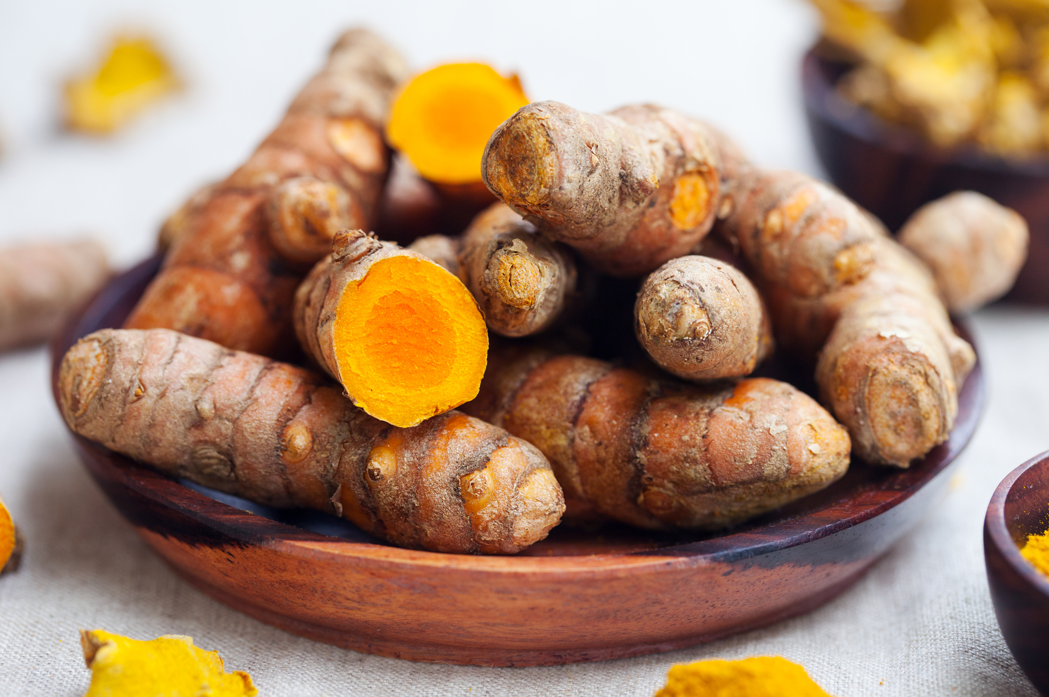 Fresh and dried turmeric roots in a wooden bowl.