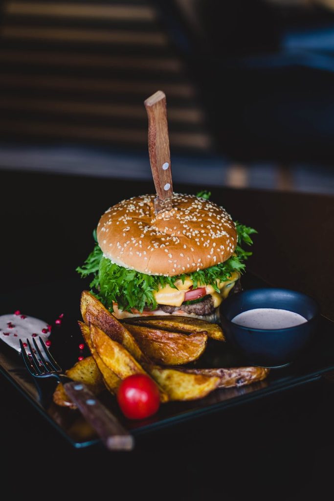 burger with fried fries on black plate with sauce on the side