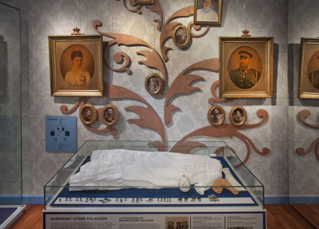Dåbskjole i montre med malerier på væggen