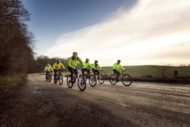 Mænd i gule veste cykler på vej.