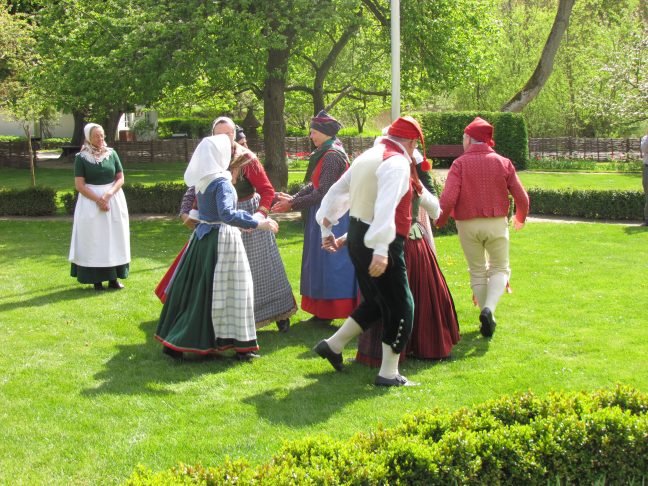 Mennesker i folkedanserdragter danser på græsplæne