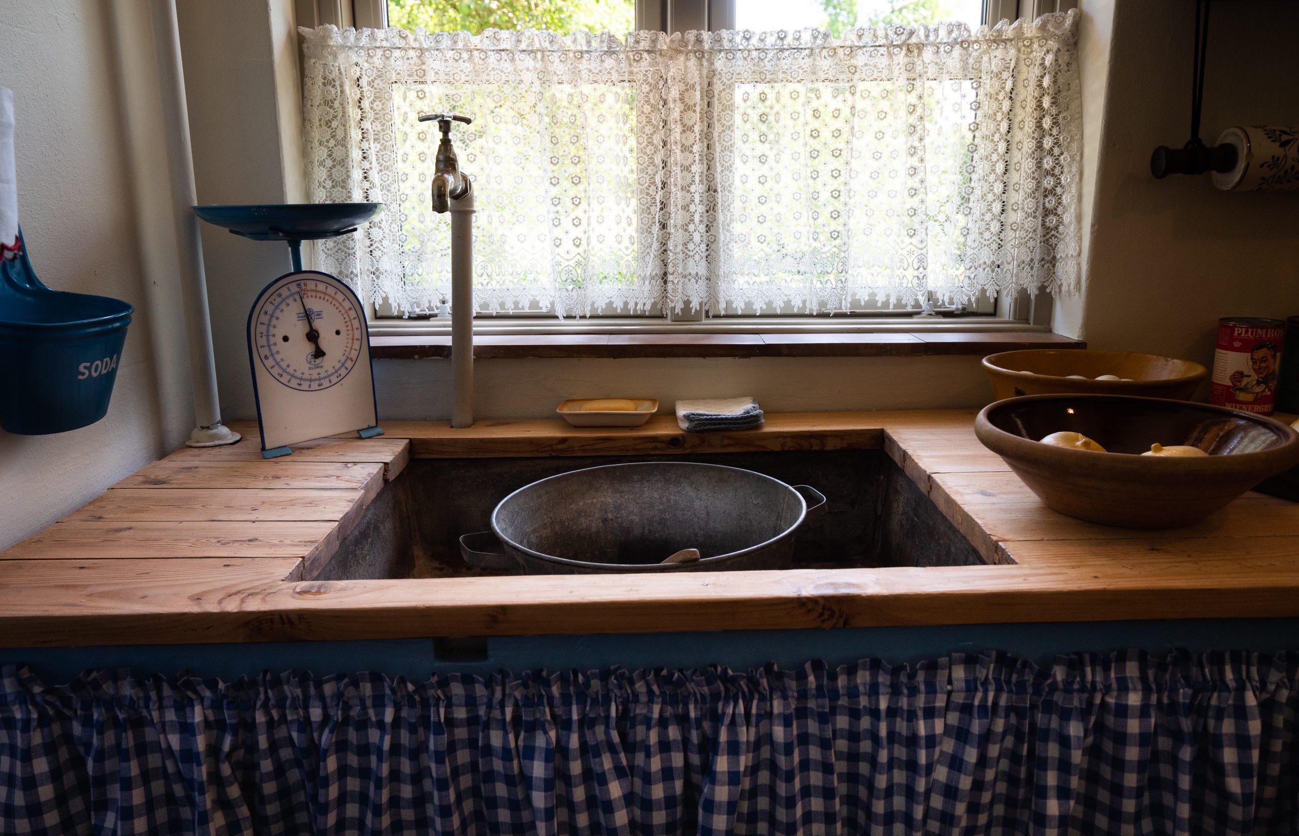 Gammeldags køkkenhåndvask og køkkenbord med frugtskål og vægt.