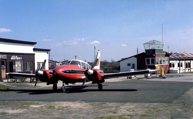 Lille rødt fly på landingsbane med bygninger i baggrunden.