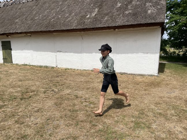 Dreng i gammeldags tøj løber på en græsplæne.
