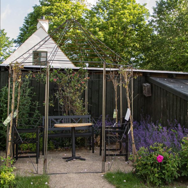 Havepavillon med møbler der står i en have med blomster.