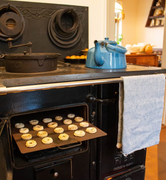 brændekomfur med blå kedel og småkager i ovnen.