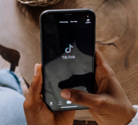 Foto met hand en gsm waar TikTok op staat.