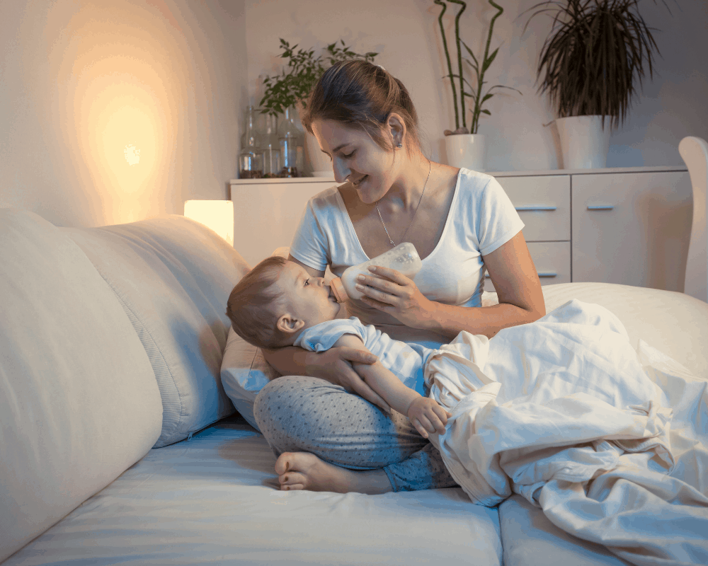 Mor som mater babyen sin med en babyflaske på sofaen