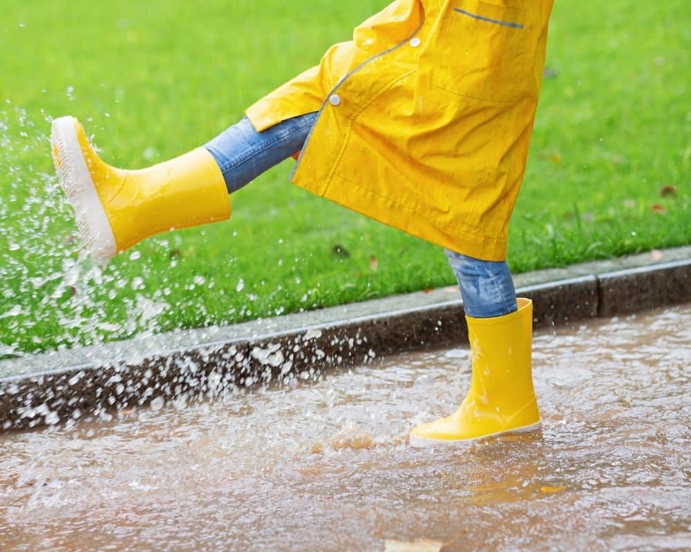 Barn med regntøy og gummistøvler som spruter i vann