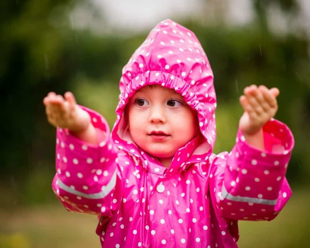 Barn med rosa regntøy føler regndråper