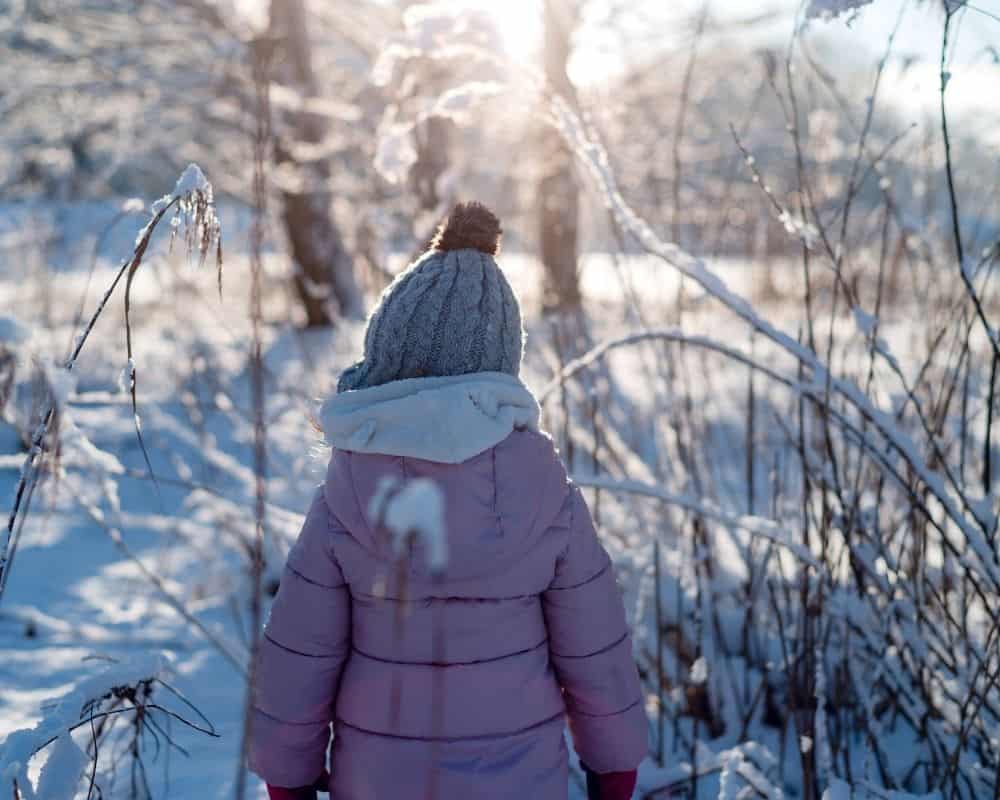 Jente med varm vinterjakke og lue i skogen om vinteren