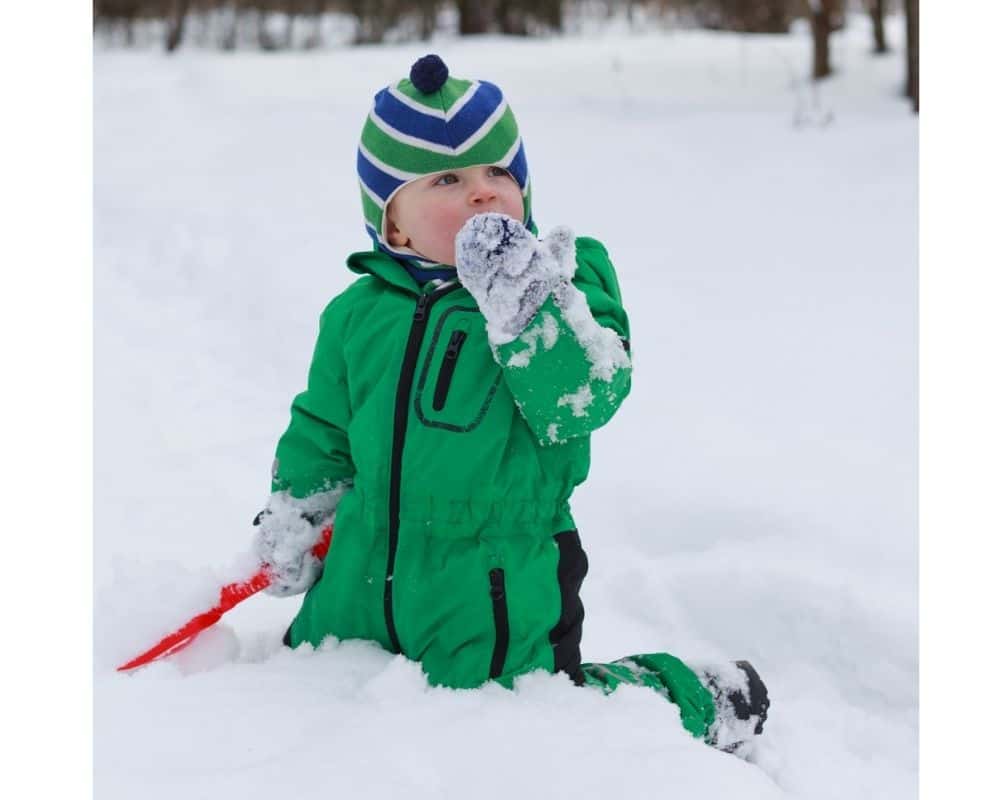 Baby med vinterdress sitter og spiser snø