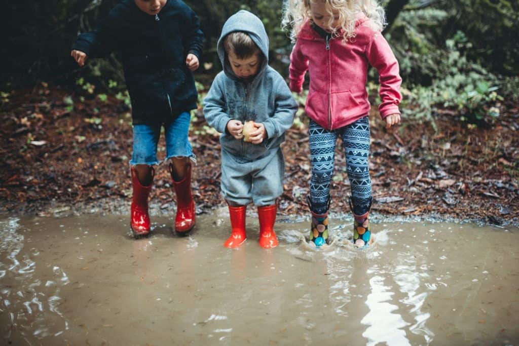 Tre barn utendørs om våren, i et stort vannbasseng på bakken