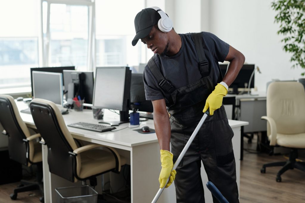 Young male staff of cleaning service company in headphones washing floor