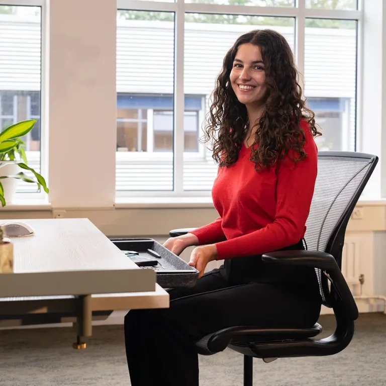 Een brunette met krullen die aan een ergonomisch bureau zit.