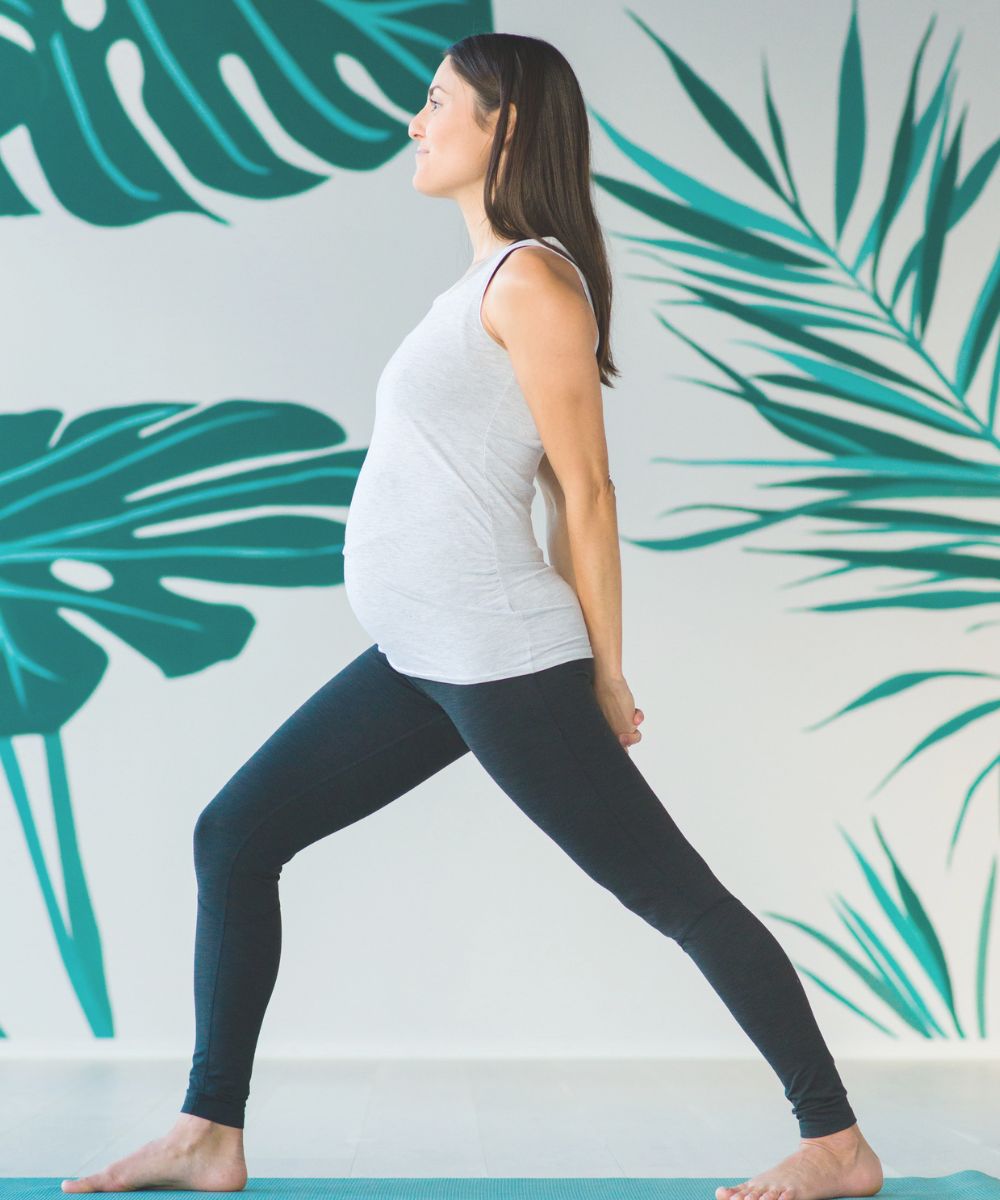 pregnant woman standing on a yoga mat practicing warrior one yoga pose for pregnancy yoga