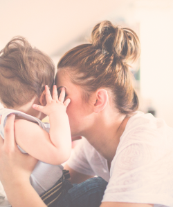 a mother holding her baby to her face. she is holding her baby close and her baby is holding her face with his hands.