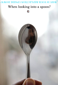 Close-up of a metal spoon reflecting an upside-down image of a person, illustrating optical distortion and identity perception.