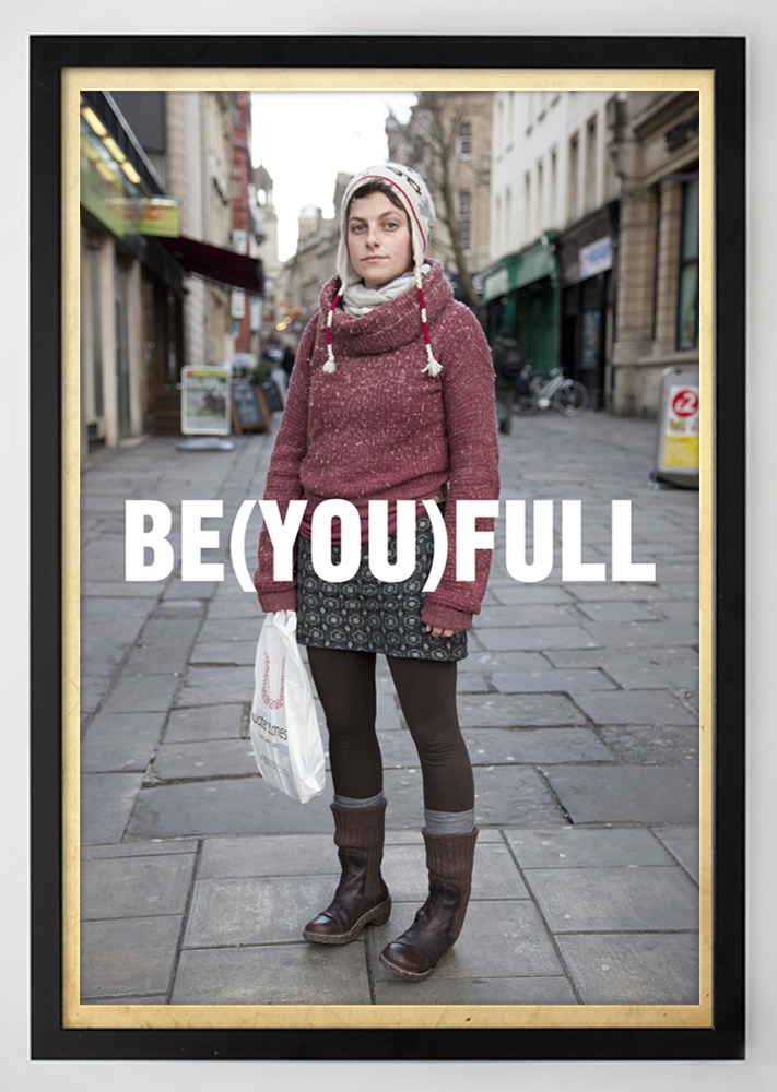 Street portrait of a young woman in a red sweater and patterned skirt standing on a city pavement, holding a plastic bag, with the bold white text “BE(YOU)FULL” across the image. Photography by Carlos Simpson Design Studio, London.