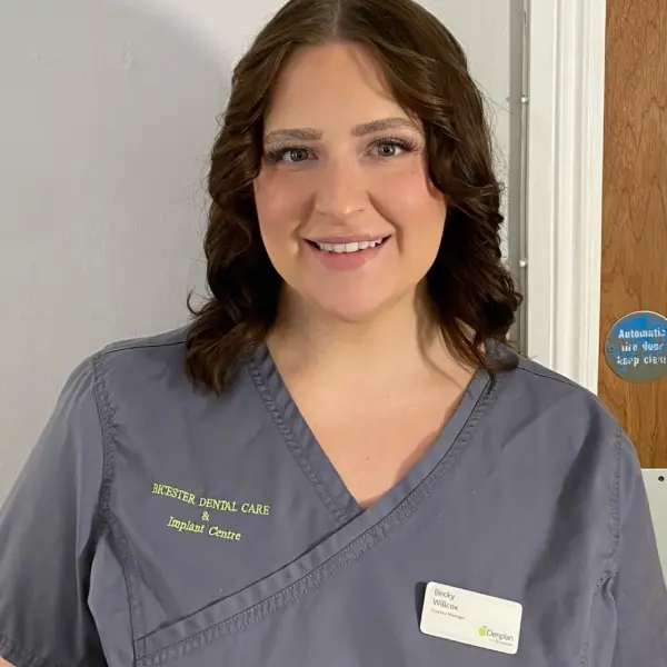 Rebecca Willcox, the Bicester Dental Practise Manager, stood in her uniform in the practise smiling to the camera. The lighting is soft and gives views a welcoming feeling.