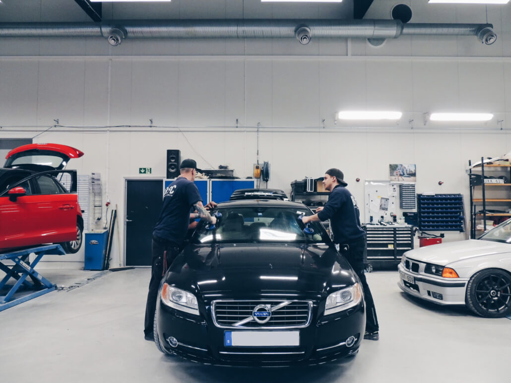 Två män reparerar glasskada på svart volvo på bilskadecentralen