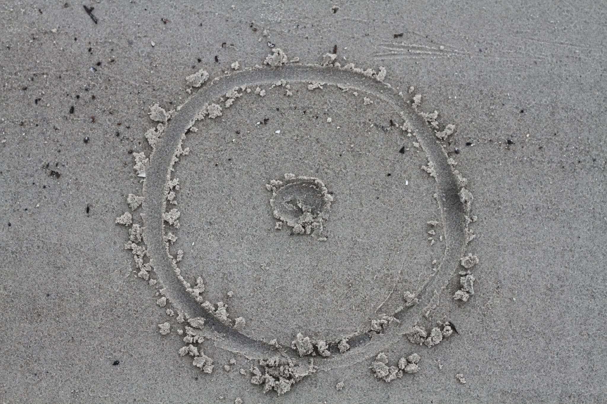 En cirkel med en prik i centrum er tegnet med en finger i vådt sand.