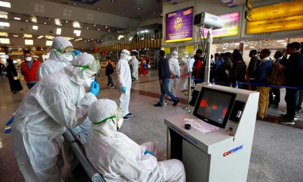 Medical staff in protective gear look at a screen while checking temperatures of passengers upon their arrival, following an outbreak of the coronavirus, at Najaf airport, in the holy city of Najaf