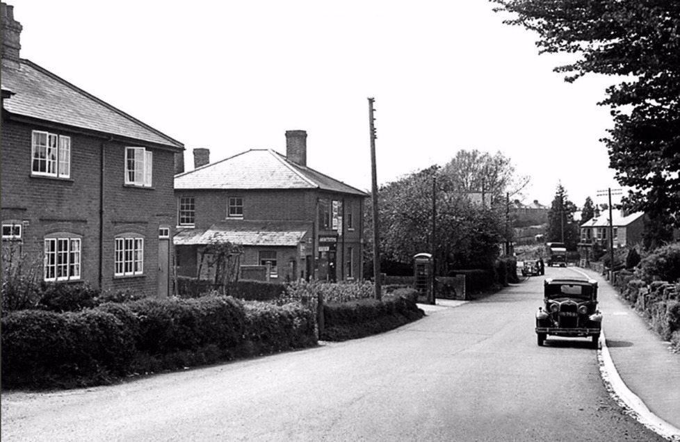 A black and white photo of a street with cars and houses Description automatically generated with low confidence