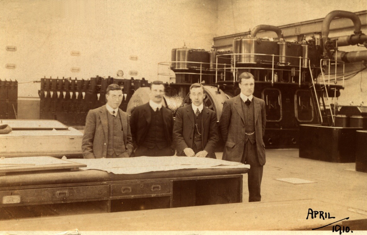 A group of men standing next to a machine Description automatically generated with medium confidence