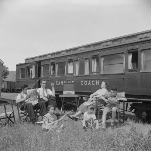 A group of people sitting on a bench in front of a train Description automatically generated with medium confidence