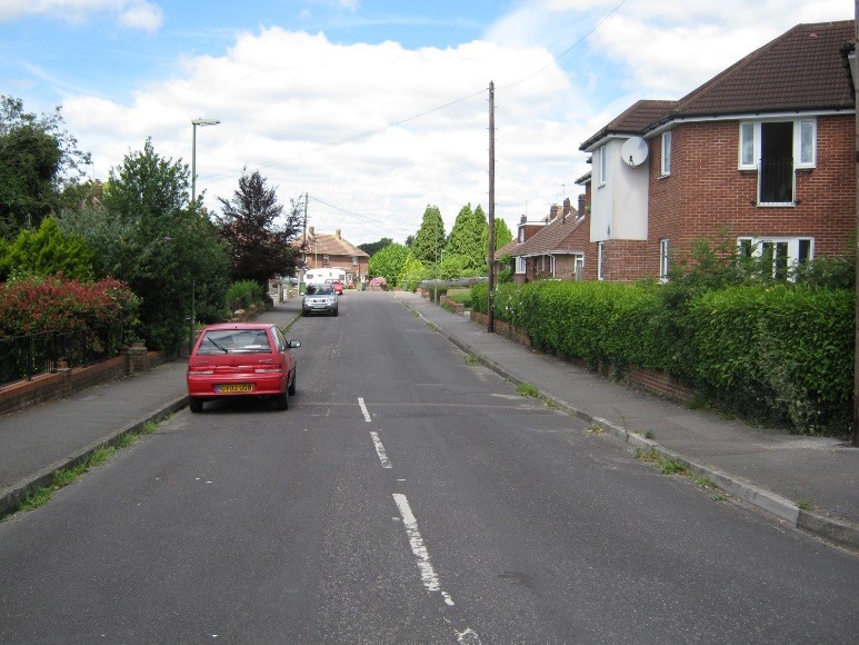 A street with cars on it and houses along it Description automatically generated with low confidence