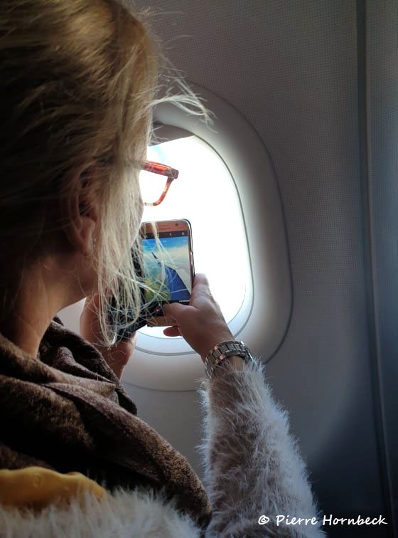 Tjej tar foto med sin mobiltelefon genom flygplansfönster