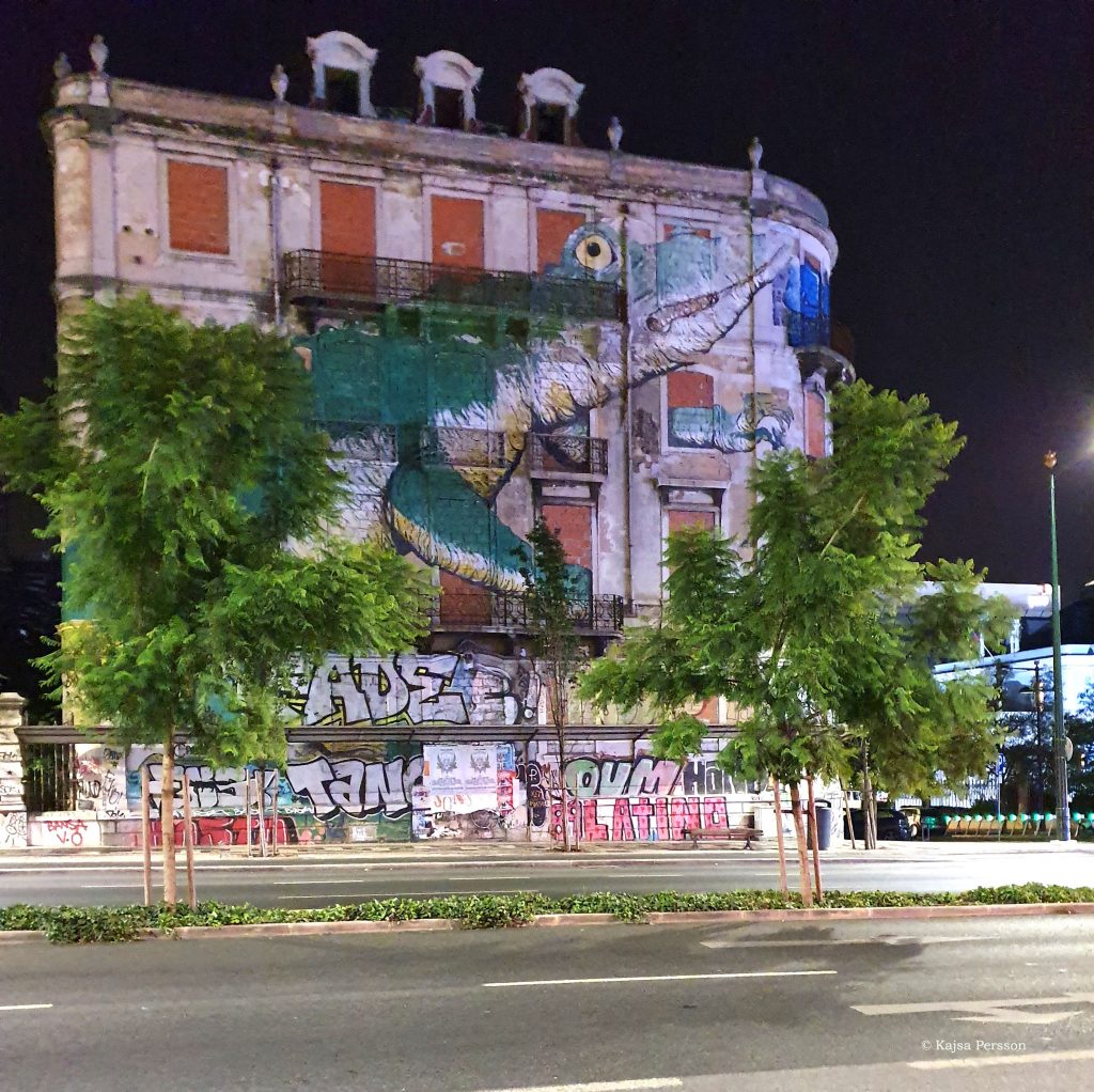 Gatukonst i Lissabon. En stor grön krokodilmålad på fasaden av ett nergånget hus