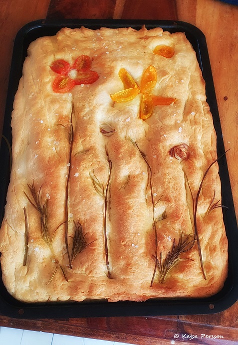 Brödbak av ett mönstrat foccacia med tomater, lök, gräslök och rosmarin som en blomsterrabatt