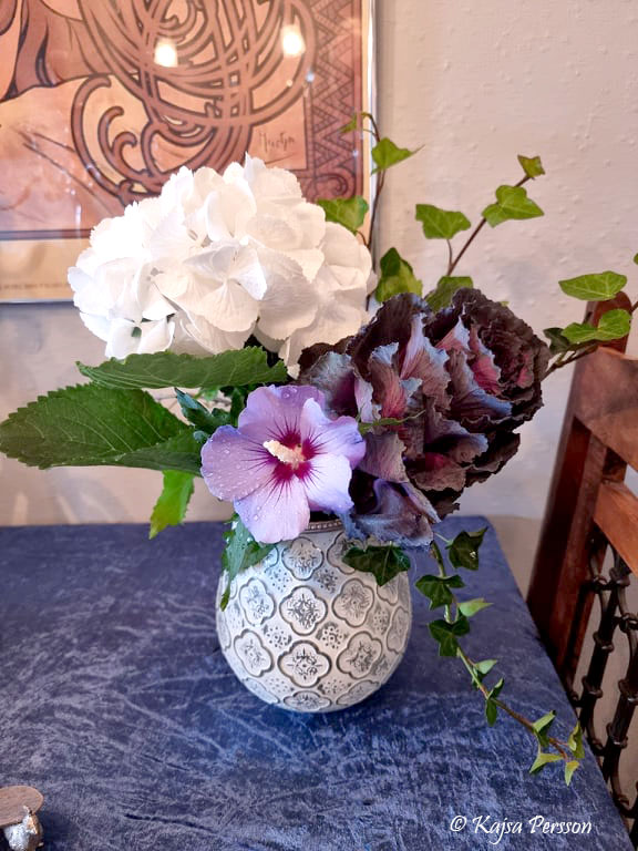 Blombukett i vit vas med kål, murgröna, vit hortensia och lila hibiskus