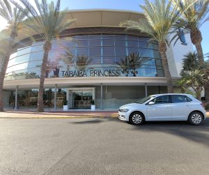 Picture of Tabaiba Princess hotel in Gran Canaria, there are 4 stars next to the hotel name and 2 palm trees at either side of the hotel. There is also a white car in front of the hotel.