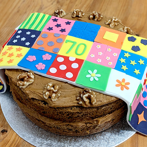 A walnut cake topped with a designed edible quilt showing the number 70.