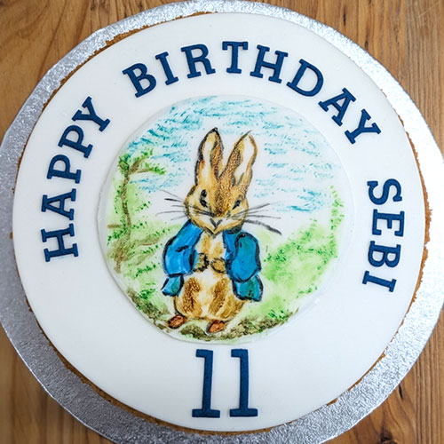 A circular sponge cake, topped with a birthday message and a picture of Peter Rabbit