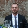 A man in business attire smiling and holding a glass, representing a positive client testimonial or a team member profile