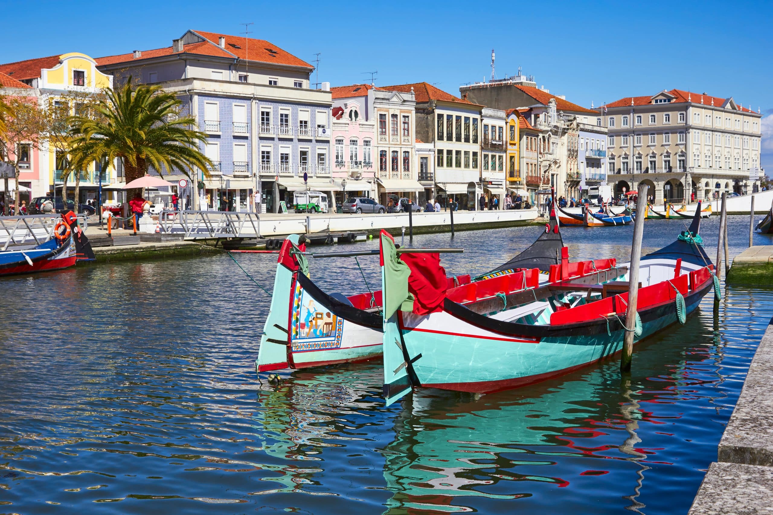 Traditional colorful boats moored along the canal in Aveiro, Portugal, with historical buildings in the background