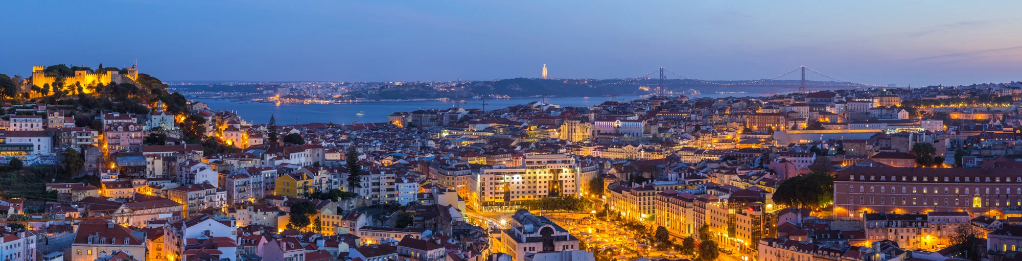 Wide panoramic night view of Lisbon showing the city lights and landmarks
