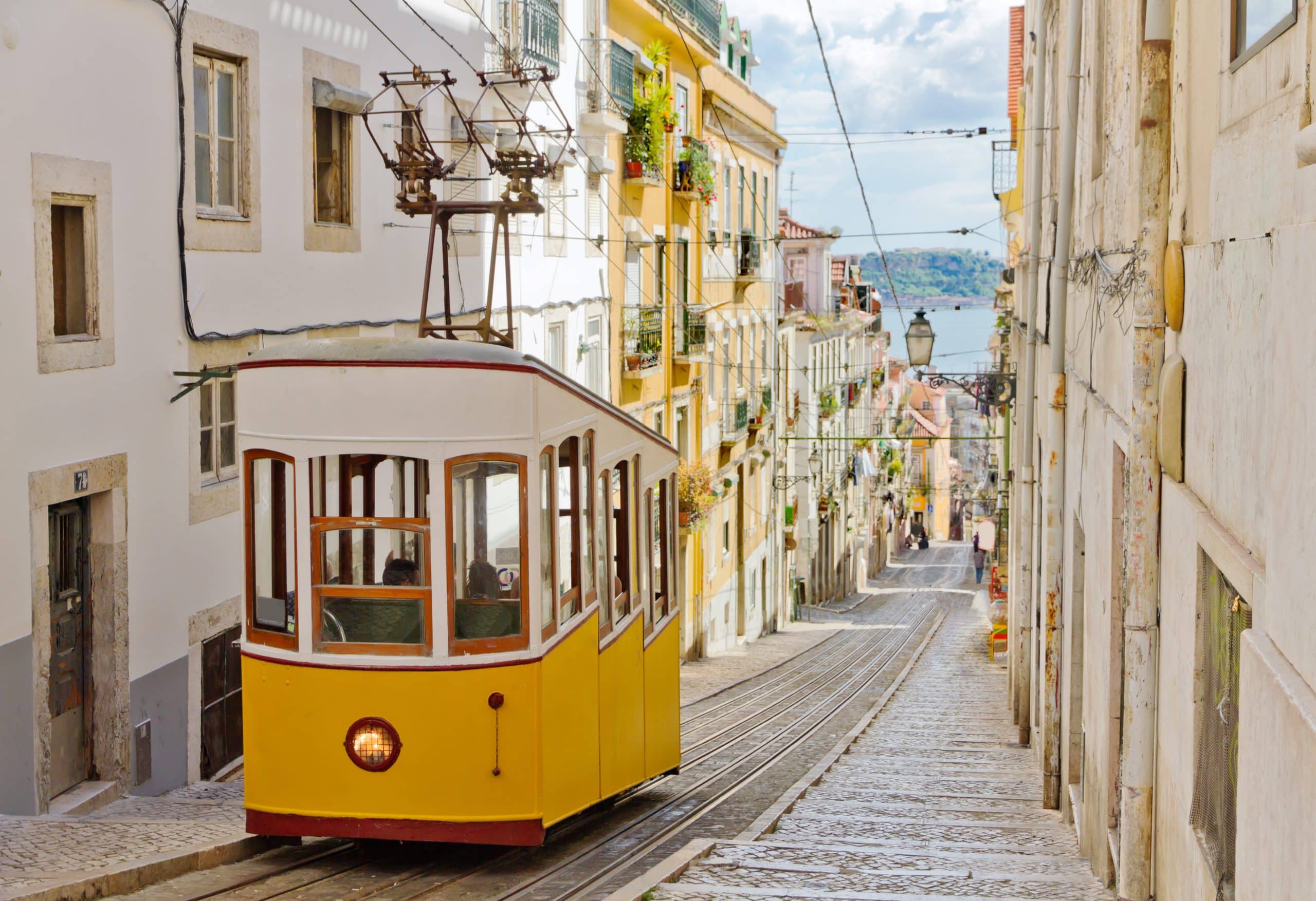 A classic yellow tram ascending a steep street in Lisbon, surrounded by historic buildings