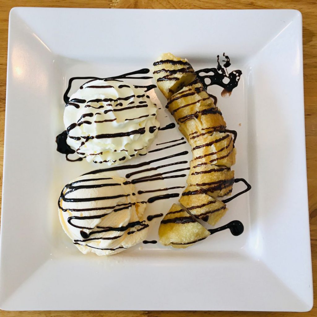 Färgstark bild av friterad banan tillsammans med glass och ett drizzle av karamellsås, serverad på en mörk skifferplatta