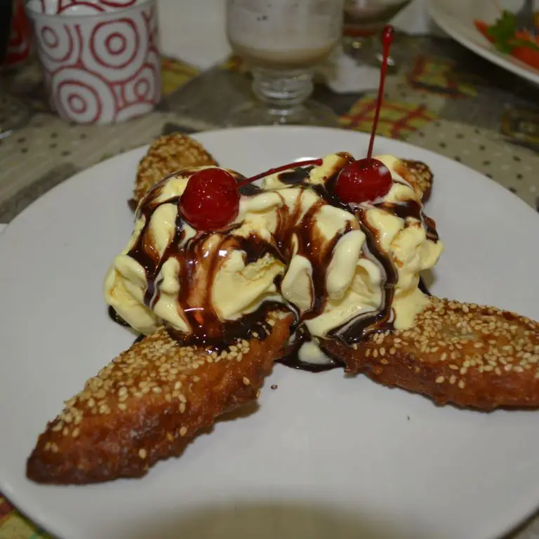 Närbild på krispig friterad banan med glass, toppad med rostade sesamfrön och färska bär på sidan