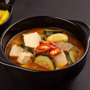 Bild på doenjang jjigae, en koreansk gryta fylld med tofu och grönsaker i en smakrik, brunaktig doenjang buljong