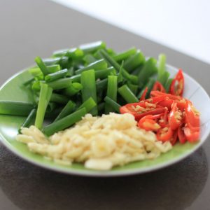 Bild på en liten tallrik med finhackad vitlök, salladslök och chili i små bitar.